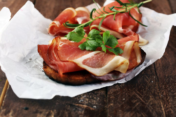 Bread with slices jamon serrano for lunch table. Sharing antipasti on party or summer picnic time over wooden rustic background.