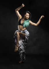 Fototapeta na wymiar beautiful strong asian with long green hair dances with sensual dramatic graceful poses on dark textured background 