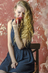 Young blonde girl with curly long hair in a polka-dot dress eating an apple
