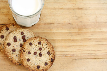 snack: glass of milk and chocolate chip cookies on wooden background, copy space