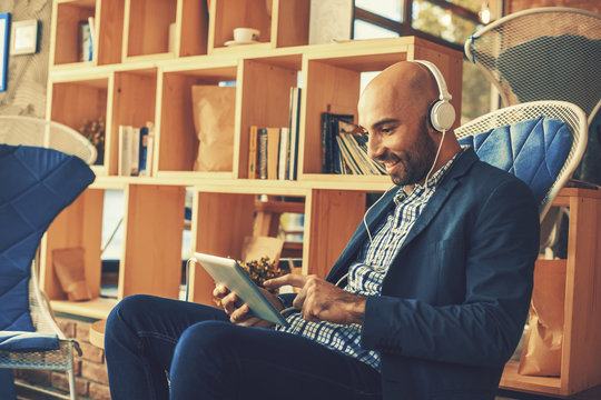 Businessman on  coffee break listening to music via digital tablet and headphones
