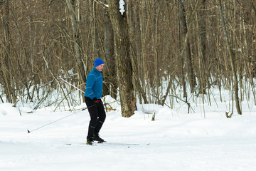 Man in a blue suit runs on skis in the winter woods.