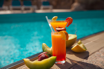 Cold cocktail near the pool in summer time with strawberry and orange