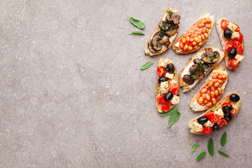 Variety of small bruschetta with caprese salad , white beans on the grill with tomato sauce and fried mushrooms with soft cheese, served on grey  background.
