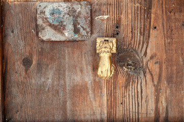 Wooden door with old golden door handle in a shape of a hand.