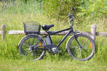 Electric bicycle on the wood fence in the park on sunny summer day. Shot from the side. Unfiltered, with natural lighting. The view of the e motor, power battery and gear.