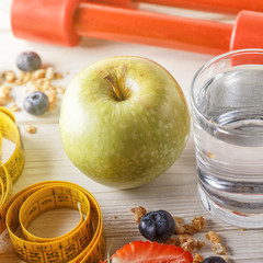 Healthy breakfast, dumbbells and measuring tape on wooden backgr