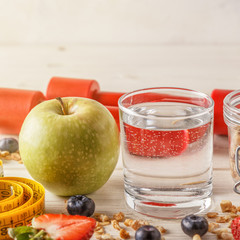 Healthy breakfast, dumbbells and measuring tape on wooden backgr