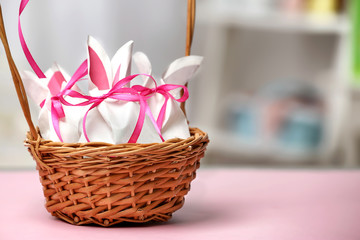 Wicker basket with paper bags in shape of Easter rabbits on table against blurred background