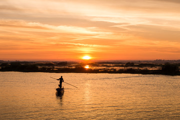 Naklejka na ściany i meble fisherman on long tail boat in the lake with sunrise background