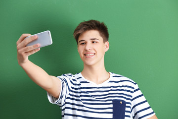 Teenage boy making selfie with mobile phone on color background