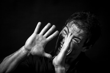 Close up portrait of isolated desparing man. Monochrome picture, black background