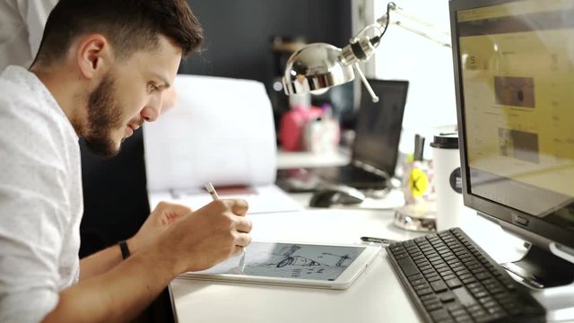 Side view of a casual male photo editor using graphics tablet in a bright office 20s 4k.
