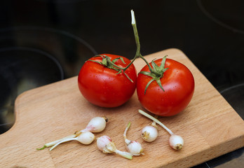 two tomatoes and young garlic on wooden cutting board