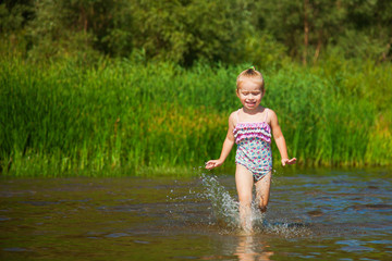 Cute little girl runs in warm water in river on a hot sunny day