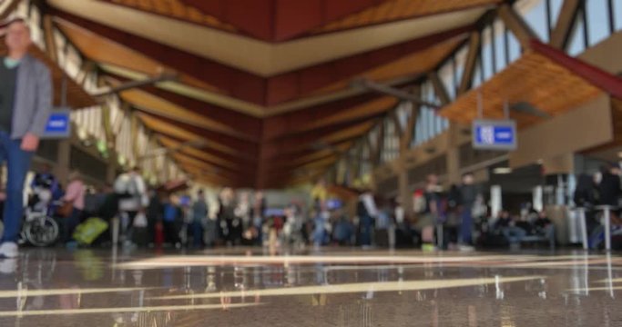 A low angle defocused shot of passengers walking around at a large airport's terminal station.  	