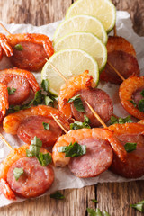 Spicy appetizer of shrimp with chorizo on skewers and herbs closeup. vertical