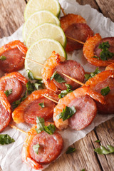 Appetizer of shrimp and chorizo on skewers and lime close up. vertical