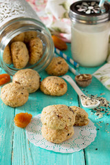 Healthy foods for breakfast. Homemade biscuits from oat flakes with sesame seeds, dried fruits, nuts in an open glass jar and milk on a wooden background. Healthy food concept.