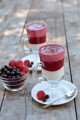 Delicious yogurt with fresh and juicy raspberry and blackcurrant in glasses near vase full of berries on wooden texture 