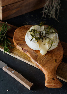 Close-up vertical shot baked cheese camembert with rosemary on a wooden tray on a rustic dark background