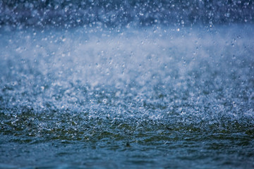 Fototapeta na wymiar raindrops running down into a puddle, splashing water visible.