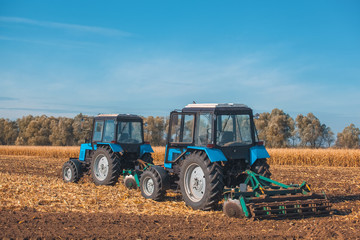 Fototapeta premium Two big blue tractor plowing a field and remove the remains of previously mown corn. The work of agricultural machinery. Harvest