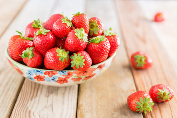 Fresh ripe strawberries in a bowl on wooden table at summer sunny day