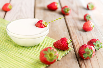 Eating healthy concept. Greek yogurt and fresh strawberries on a wooden table at sunny day.