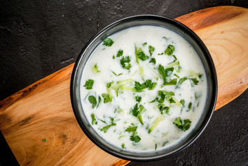 Summer diet cold soup tarator, yogurt with cucumbers and greens on a black concrete stone table