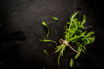 Bunch of salad leaves (greenery), arugula, black concrete stone table, top view