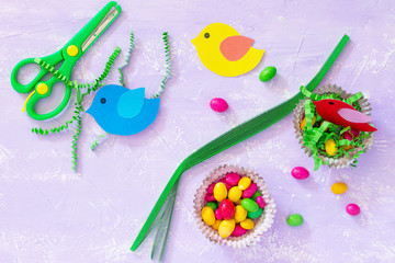 Creating children's Easter table. Paper quilling, paper nest, bird, painted eggs and sweets on the festive table.