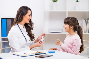 Female doctor showing inhaler to a child at the medical office.