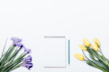 Lilac irises, yellow tulips and notepad with a pencil on a white table