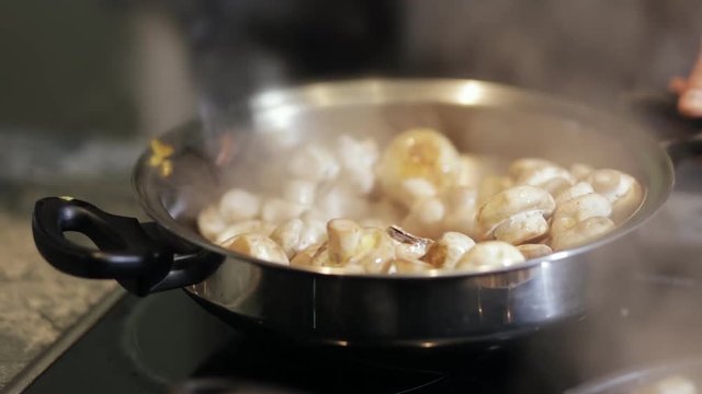 Close-up of chef hands mixing roast mushrooms on pan in kitchen