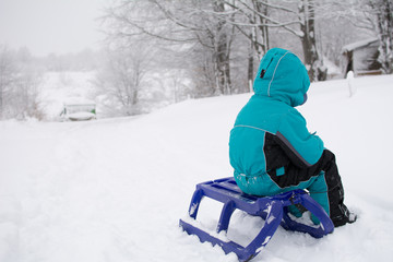 Fototapeta na wymiar Little boy sitting on a sleigh. Around a lot of snow. Winter landscape on mountain.