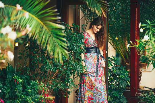 beautiful brunette woman in a colorful dress standing on the porch of his villa in the jungle