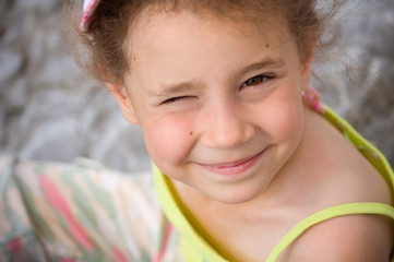 Portrait of a cute baby girl in summer near the sea. The girl smiles and squints from the sun.