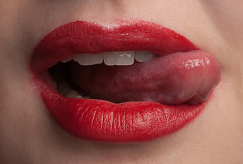 Detail of young female licking her red lips.