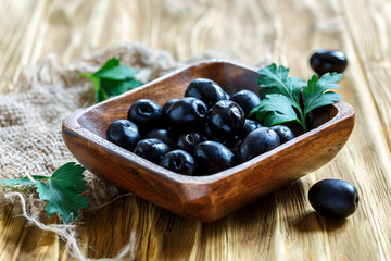 Black olives in a square wooden bowl and a sprig of parsley.