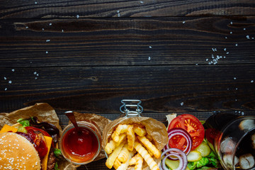 Fresh delicious burgers with french fries, sauce and drink on the wooden table top view, with copy...