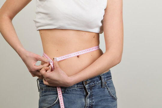 Weight loosing: Young woman in jeans measuring waist with tape on a white background