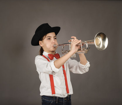little girl playing trumpet on a gray background