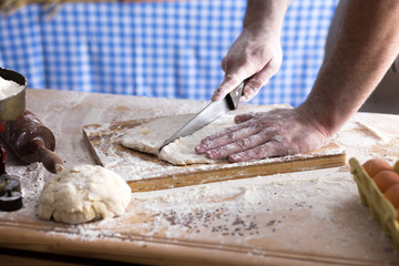 Close up of male baker hands cutting dough with knife and making bread.