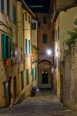Fototapeta na wymiar Medieval narrow cozy street in Siena at night, Tuscany, Italy