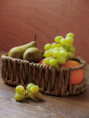 Basket with grapes pears and oranges on a wooden table, 
