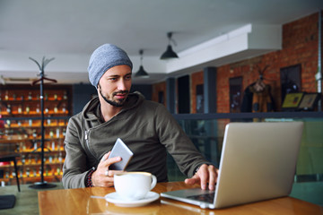 Young handsome hipster man with beard is using computer in cafeteria