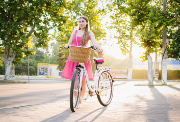 Young woman with city bike going in the park at sunrise or sunset