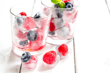 glass with frozen berries in cubes on wooden desk background
