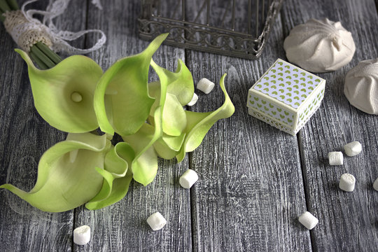 bouquet of green yellow calla lilies with marshmallows and cardboard box on a gray wooden background.